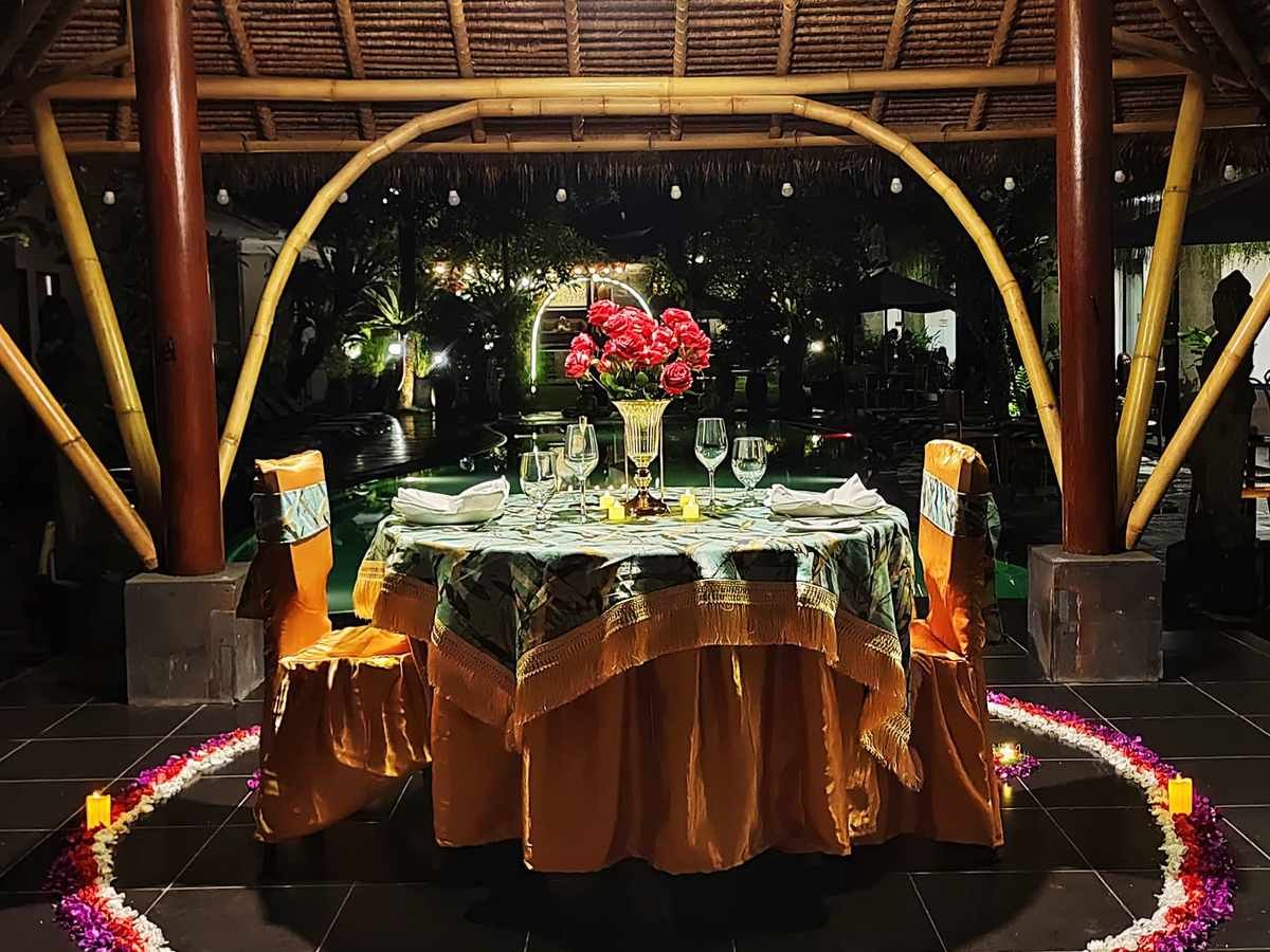 A candlelit table for two under a bamboo arch beside the pool