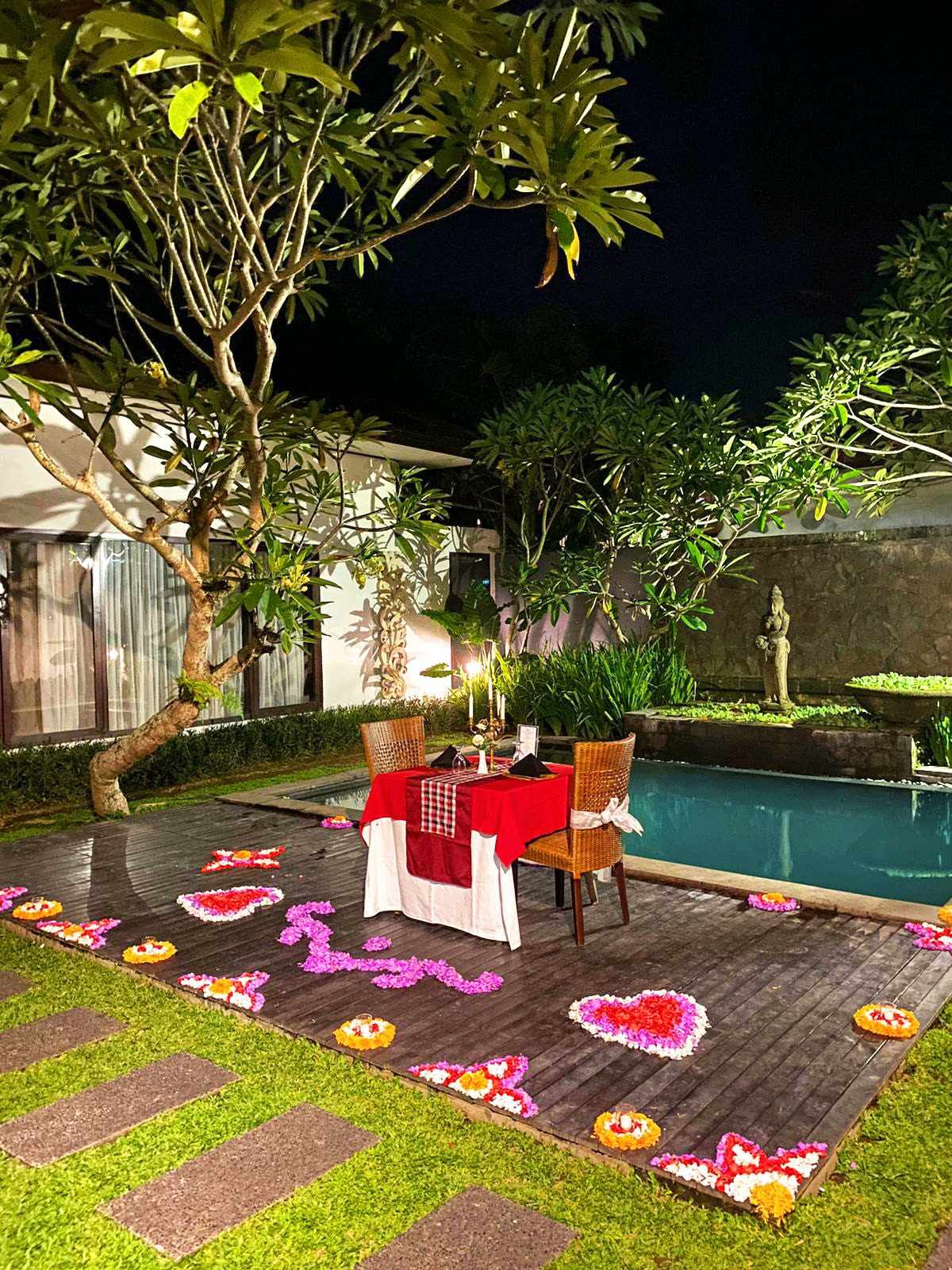 A table dressed with flowers beside a private villa pool at night